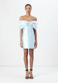 Abito blu chiaro off-shoulder con un grande fiocco sul davanti, realizzato in satin liscio. Lunghezza corta, silouette aderente, abbinato a tacchi neri con cinturino alla caviglia.