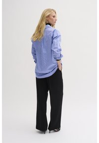 Blue and white striped button-up shirt, relaxed fit, long sleeves. Paired with high-waisted black wide-leg trousers and black heels.