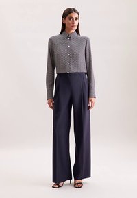 Grijs patroon overhemd met knopen en een kraag, gecombineerd met marineblauwe wijde broek met hoge taille. Zwarte sandalen met bandjes maken de outfit compleet.