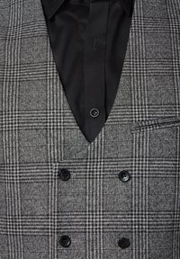 Dwurzędowa kamizelka w czarno-białą kratę. Posiada dekolt w serek, dwa czarne guziki oraz gładką, teksturowaną czarną koszulę pod spodem.