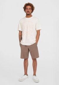 Crewneck-T-Shirt in Off-White mit pinkem Grafikdruck, kombiniert mit hellbraunen Shorts und weißen Sneakern. Lässige Passform und aus Baumwollmaterial.