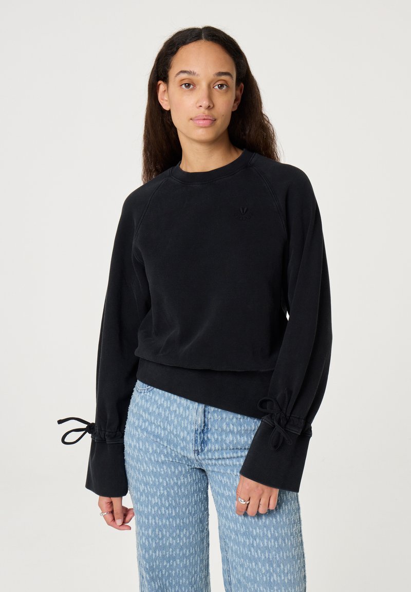 Zwarte cropped sweatshirt met lange mouwen en strikdetails bij de manchetten, gemaakt van zachte stof. Gecombineerd met lichtblauwe gemusterde jeans.