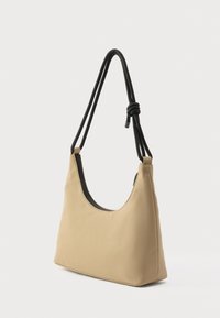 Bézs színű szövet táska ívelt formával, fekete állítható pánttal és a tetején cipzáras záródással. Simább textúra, minimális díszítéssel.