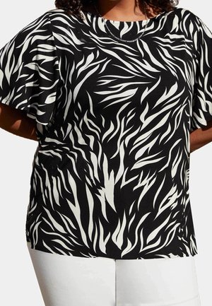 Sort-hvid abstrakt zebra-mønster kortærmet bluse båret med hvide bukser og en tynd kæde halskæde.