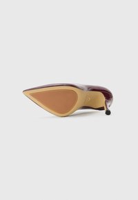 Chaussure à talon aigu maroon, vue depuis la semelle, avec une semelle en caoutchouc beige et un talon fin, sur fond blanc.