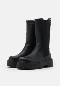 Svarta läderchelsea-boots med elastiska sidor, chunky svarta gummiplattformssulor och en slät yta.