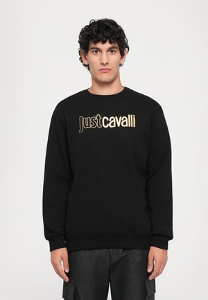 Svart crewneck sweatshirt med gullfarget "Just Cavalli"-logo på fronten. Myk stoff, ribbestrikkede mansjetter og hem, kombinert med mørke cargo-bukser.