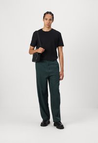 Sort kortærmet T-shirt parret med mørkegrønne fløjelspants. Outfitet er suppleret af sorte sko og en lille sort skuldertaske.