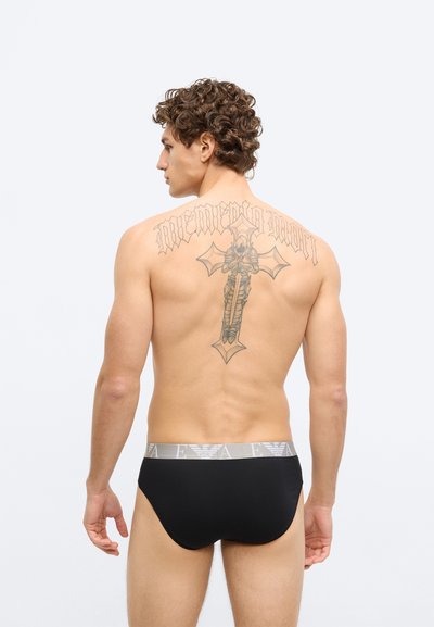 Fekete fehérnemű szürke logós derékpánttal, sima textúrával és testhezálló szabással. A háton jól látható tetoválás díszíti.