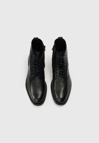 Ghete negre din piele cu finisaj neted, design cu șireturi, fermoar lateral și detalii subtile perforate pe părțile laterale.