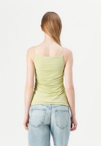 Lichtgroene, aansluitende tanktop met dunne randen, voorzien van geplooide textuur aan de achterkant. Gekoeld met lichtblauwe denimshorts.