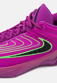 Sportsko med en lilla stofoverdel med grønne linjer og sorte detaljer. Glat tekstur med en syntetisk sål og snørebåndsdesign.