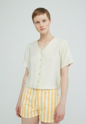 Beige blouse met korte mouwen en v-hals, voorzien van knopen, gecombineerd met gele en witte gestreepte shorts. Zachte stof en ontspannen pasvorm.