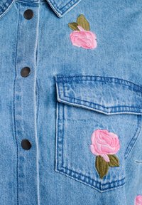Helehelesinine denim särk mustade nupudega, rinna tasku ja roosa roosi tikandiga koos roheliste lehtedega ees.