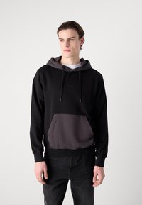 Felpa con cappuccio nera, con una tasca e un cappuccio grigi a contrasto. Realizzata in tessuto morbido con cordini regolabili. Polsini elasticizzati.