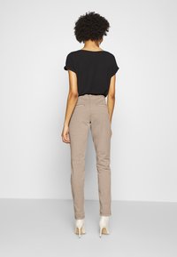 Czarna, krótkiego rękawa bluzka w połączeniu z beżowymi, spodniami z wysokim stanem. Spodnie mają dopasowany krój i dwie tylne kieszenie. Noszone z jasnymi obcasami.