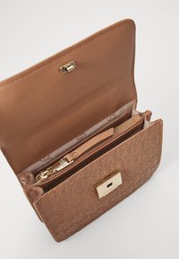 Brown patterned handbag with a textured surface, gold hardware, and zipper compartments. Opens with a clasp, featuring a sleek, structured shape.