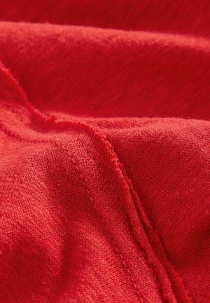 Roter Stoff mit einer weichen Textur, der sichtbare Nähte und Falten aufweist und eine reiche, einheitliche Farbe ohne Muster oder Akzente zeigt.