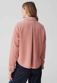 Pink corduroy shirt with vertical stripes, long sleeves, and a shirt collar. Features a relaxed fit and a curved hem at the back.
