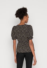 Blusa preta com padrões florais, com mangas bufantes, cintura franzida e decote arredondado, apresentando pequenos padrões florais multicoloridos por toda a peça.