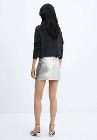 Jupe mini argentée métallisée avec une texture lisse et une fermeture éclair à l'arrière. Stylisée avec un pull sombre et des sandales à talons métalliques.