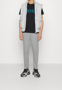 Ljusgrå ärmlös väst över svart t-shirt med "BOSS" i teal, ihop med grå sweatpants och svart/vita träningsskor.