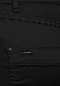 Il tessuto di denim nero presenta un primo piano di una tasca, con un accento in metallo argentato e un piccolo etichetta che legge "street one".