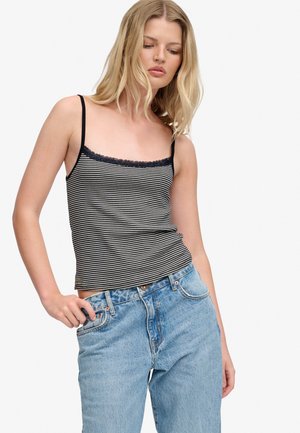 Ung kvinde iført en sort og hvid stribet camisole med blondet kant og lyseblå cowboybukser med høj talje, der kigger ned.