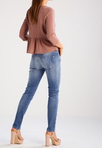 Rosa peplumtop med ¾ ärmar i kombination med ljusblå skinny jeans och nudefärgade platåklackar, vilket visar en avslappnad passform och rena linjer.