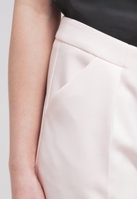 Lichtroze op maat gemaakte broek met een gestructureerde afwerking, voorzien van een flatte front en zijzakken. De stof is glad en gestructureerd.