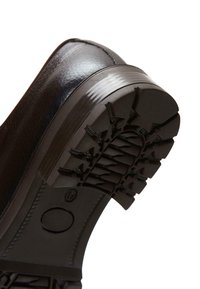 Zapato de cuero negro con suela de goma texturizada y un patrón de piso robusto, que proporciona agarre y durabilidad.