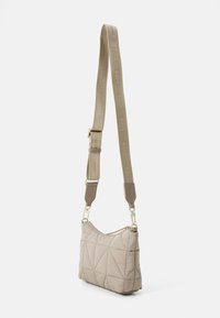 Bolso de hombro beige acolchado con forma curva, que presenta una tela texturizada, herrajes en tono dorado y una amplia correa con logotipo.