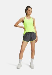 Neón žltý tank top s čiernymi akcentmi a šedými športovými šortkami s neónovo zeleným lemovaním. Model má na sebe biele topánky a ponožky po členky.