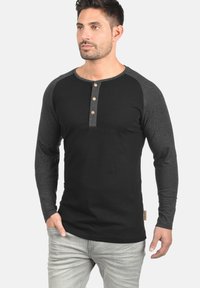 Crna majica dugih rukava sivi raglan rukavi, s henley ovratom i četiri drvene tipke. Mekani pamučni materijal.