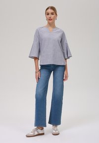 Stripet blå og hvit bluse med V-hals og bell sleeves, kombinert med lyseblå vide bukser og beige sneakers.