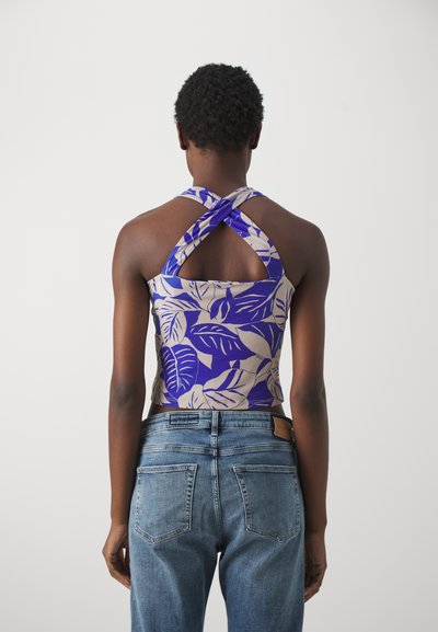Top court violet et beige avec un motif de feuilles, présentant un design à dos croisé. Assorti à un jean en denim bleu clair avec poches arrière.