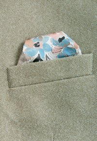 Beige strukturierter Stoff mit einem Einstecktuch, das ein florales Muster in Blau, Pink und Schwarz zeigt. Einstecktuch teilweise sichtbar.