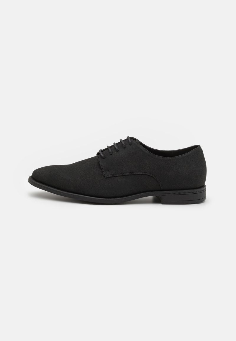 Chaussure Oxford en suede noir avec une texture lisse, un bout arrondi et six œillets pour les lacets ; semelle en caoutchouc noir à profil bas avec des accents subtils.