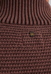 Sweter dzianinowy z prążkowanym kołnierzem w ciemnym brązie, teksturowanym tkanym ciałem w jaśniejszym brązie oraz małą czarną metalową metką z napisem "PME LEGEND."