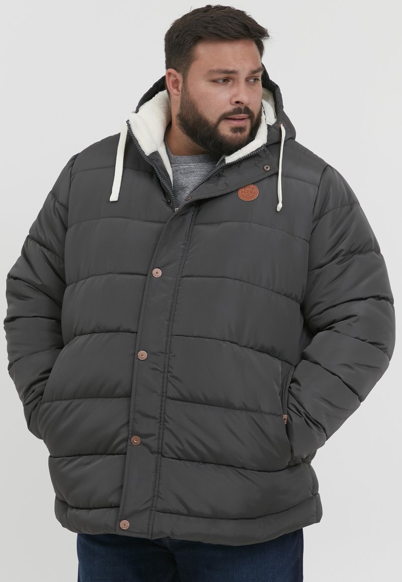Padded gray jacket with a hood, featuring a fleece lining, button closures, and a brown logo patch. Designed for warmth and comfort.