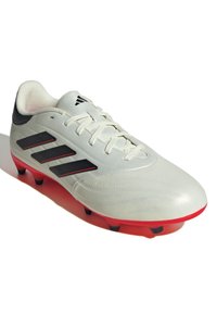 Botas de fútbol blancas con acentos en negro y rojo, que presentan tres rayas negras, un upper sintético liso y una suela roja con tacos negros.
