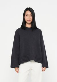 Dunkelgrauer gestrickter Pullover mit Rundhalsausschnitt, weiten Ärmeln und geripptem Saum. Hergestellt aus strukturiertem Stoff, mit lockerer Passform und überschnittenen Schultern.