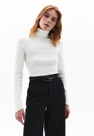 Witte geribde coltrui gecombineerd met hoog-welfde zwarte broek, vastgemaakt met een zwarte riem met een goudkleurige gesp.