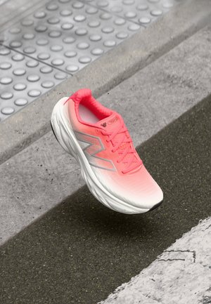Une chaussure de course unique rose néon et blanche flottant au-dessus d'un trottoir texturé et d'une surface de route en asphalte.
