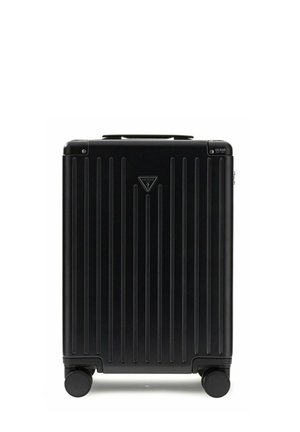Valise rigide noire avec des rainures verticales, quatre roues, poignée supérieure et logo Guess au centre et dans le coin supérieur.