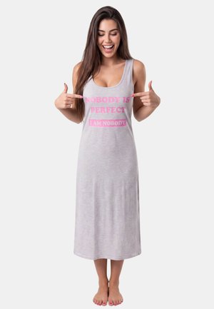 Vrouw in een grijze mouwloze jurk die lacht en wijst naar roze tekst met de tekst "NOBODY IS PERFECT I AM NOBODY" aan de voorkant.