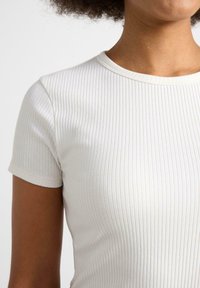 Vit ribbad t-shirt med kort ärm, med rund halsringning och slimmad design, som framhäver en slät yta och subtila ränder.