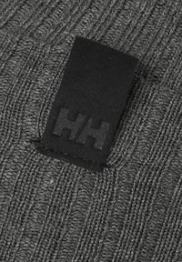 Šedá pletená tkanina s ribkovou strukturou, která má připevněnou černou obdélníkovou nášivku s embosovaným logem "HH".