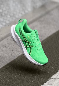 Neon green athletic shoe with a textured mesh upper and white sole, featuring black and gold accents and a traditional lace-up design.
