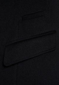 Czarny wełniany płaszcz z detalem pokazującym elegancką kieszeń z złożonym klapkiem i subtelnym przeszyciem, prezentując gładki, teksturowany materiał.